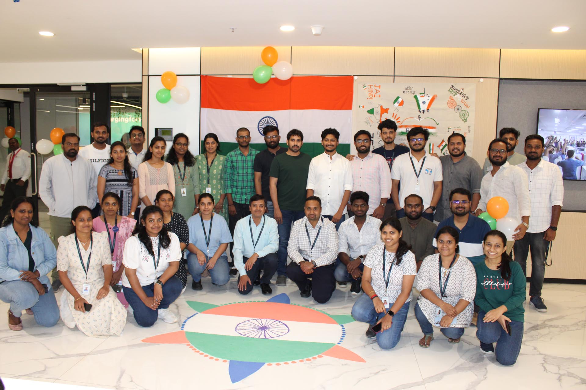 A group of people smiling and posing together in front of a large Indian flag.
