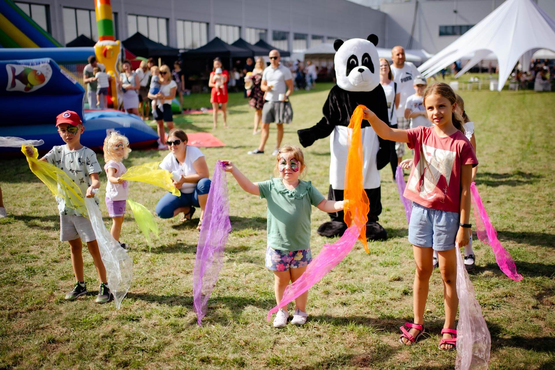 a group of kids standing in a field with a person in a panda garment