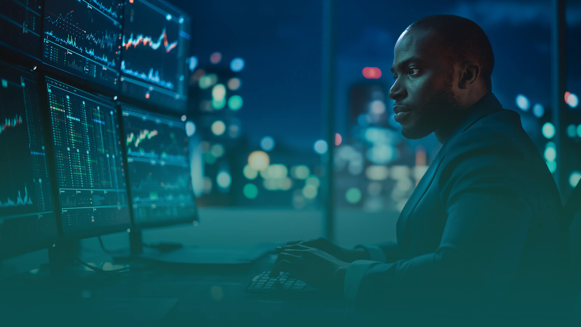 a man sitting in an office at night looking at computer screens