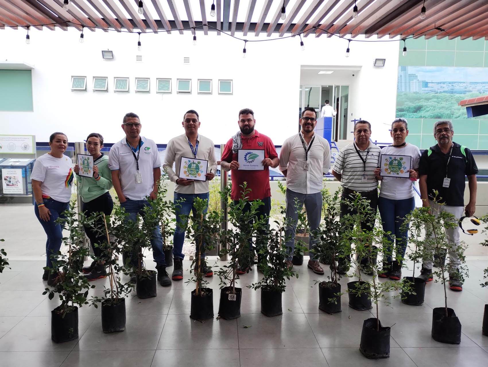 Group of people holding certificates standing behind a row of trees yet to be planted