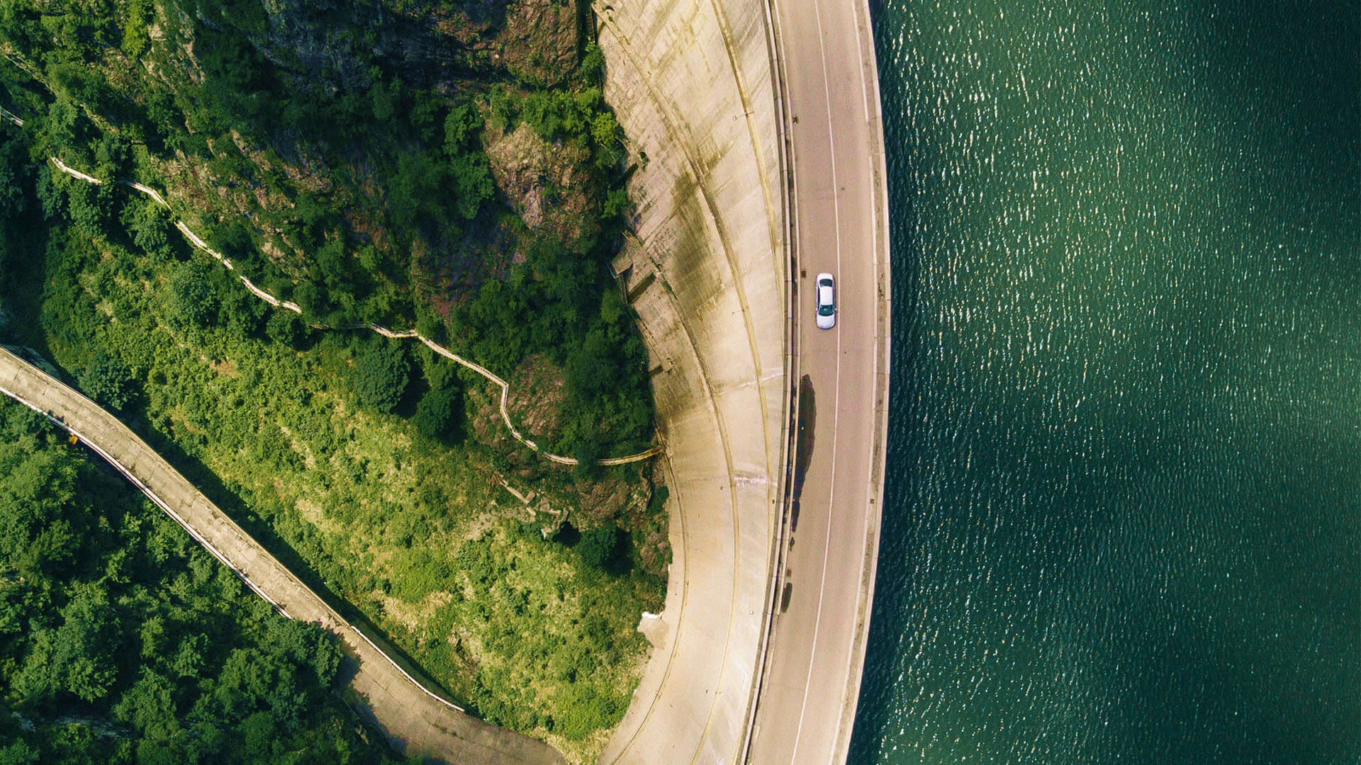 Vehicle driving up on a road between a lake and a wood