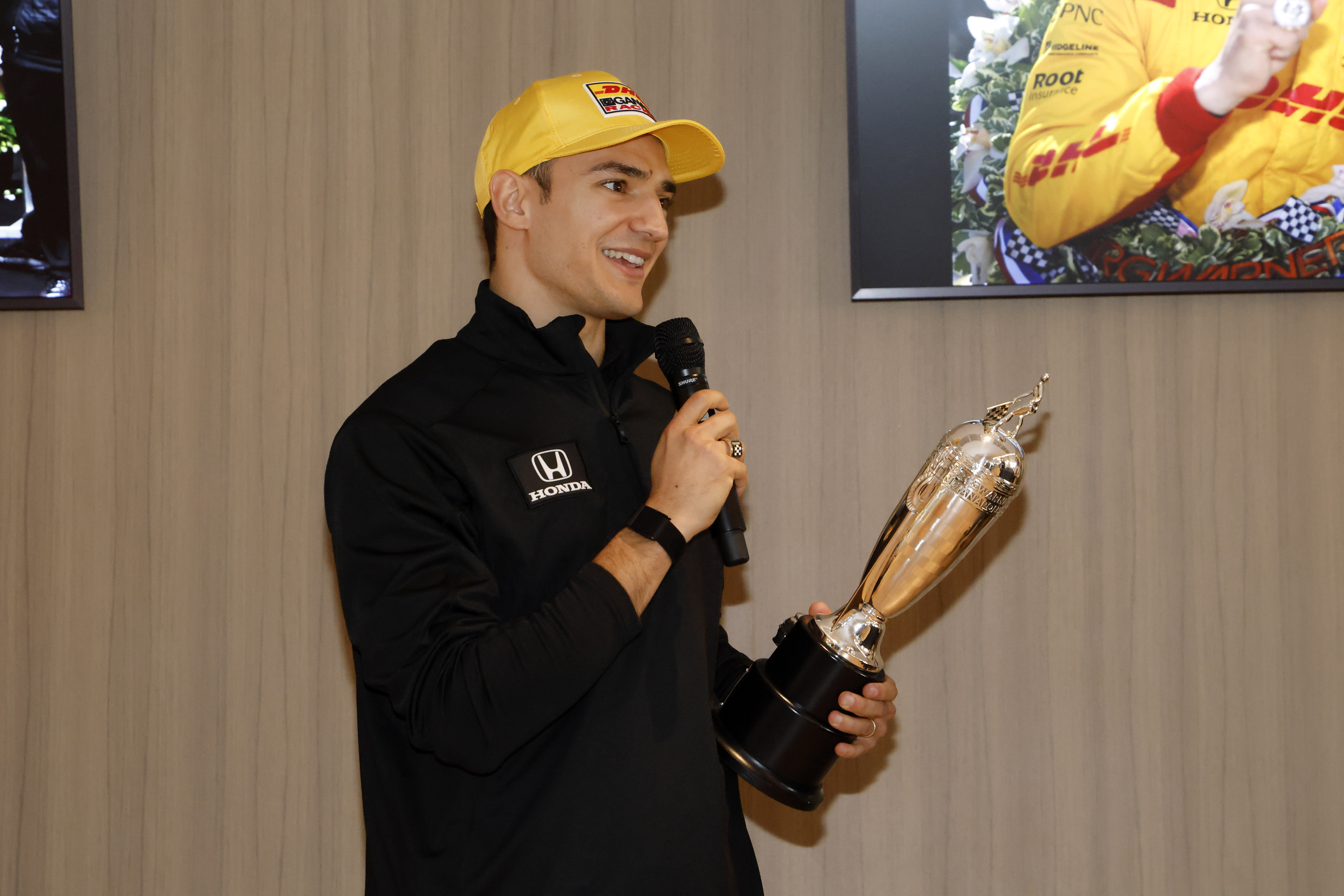 Man speaks into microphone while holding a trophy