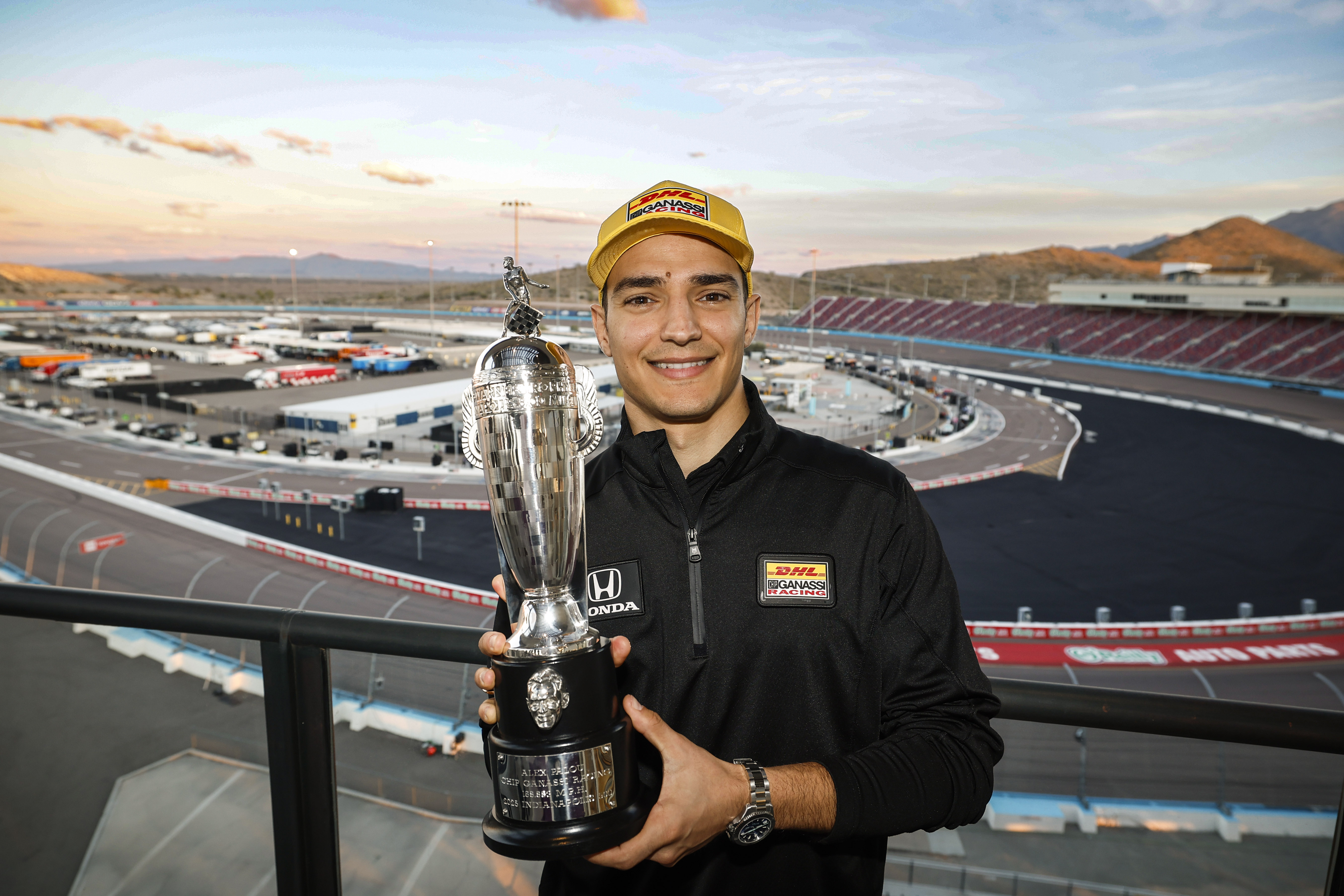 Man holds trophy and smiles in front of race track