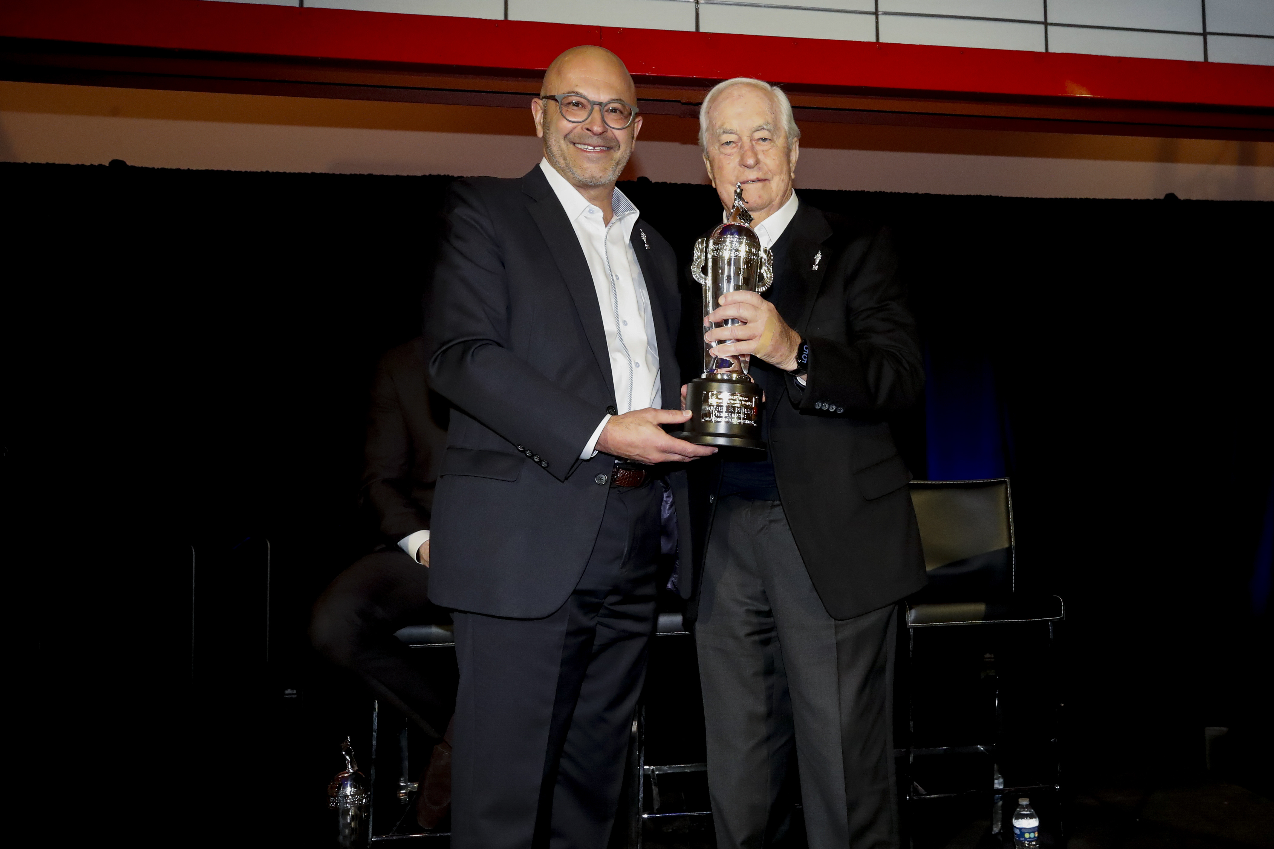 Two men smile while holding a trophy